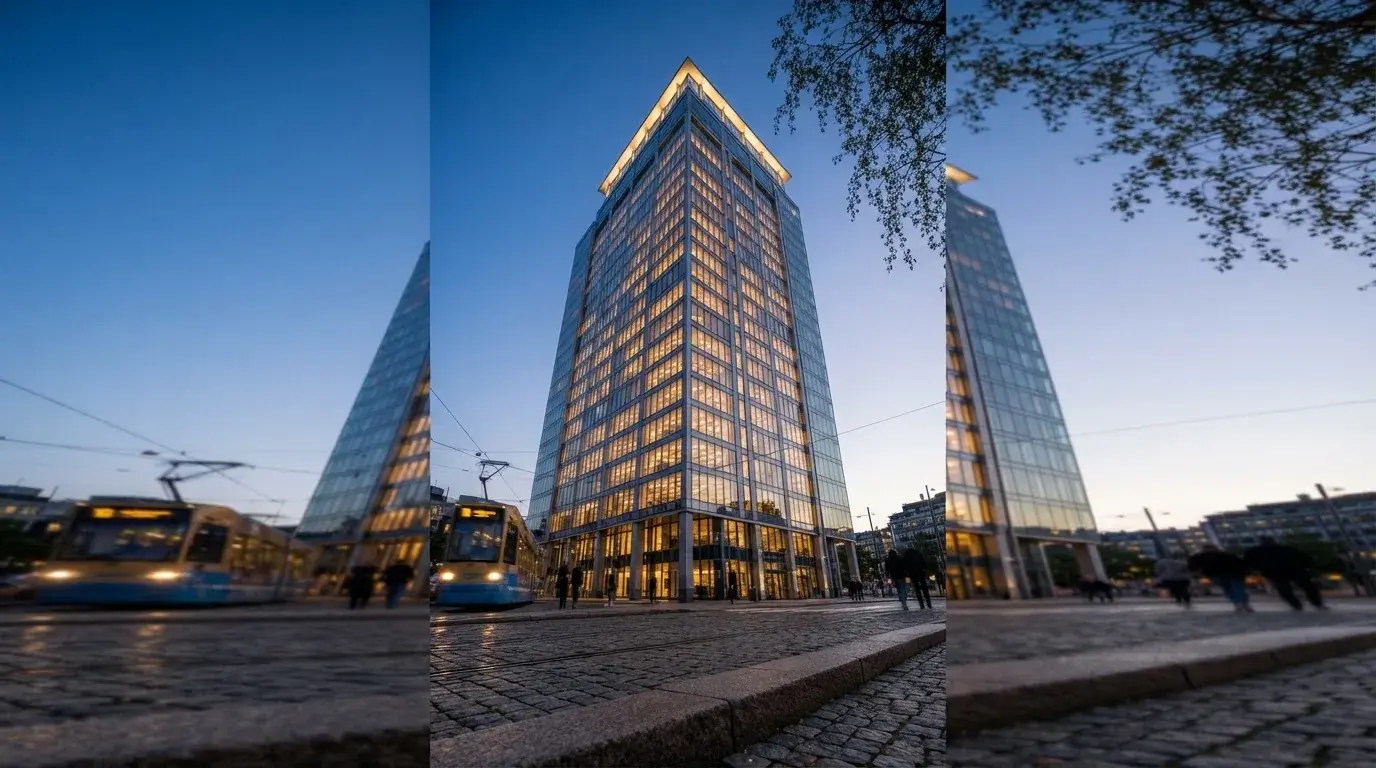 En modern kontorsbyggnad i skymning fotograferad underifrån med tända fönster mot en klarblå himmel i en svensk stad.